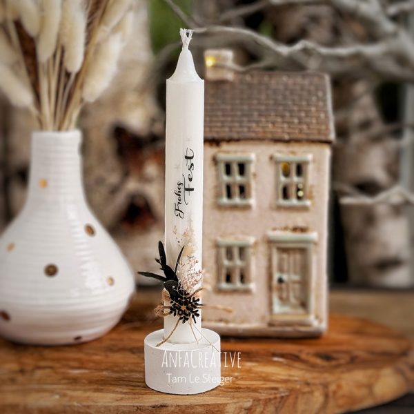 Weiße Weihnachtskerze mit dem Schriftzug „Frohes Fest“, Hirschmotiv, grünen Blättern und zarten Blüten.